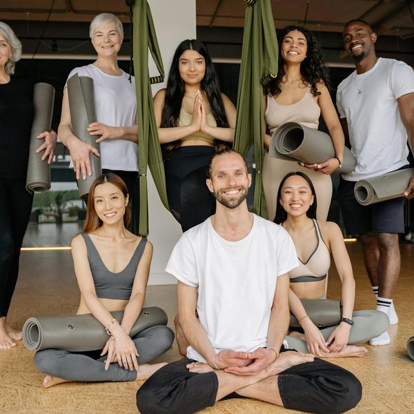 A diverse group of people smiling and preparing for a yoga class in a bright studio.